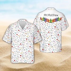 May include: A white short-sleeve button-down shirt featuring a colorful pattern of school supplies, math equations, and the word Teacher. The back displays the text Mr. Matthew above a row of illustrated crayons in various bright colors.