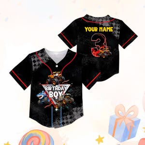 May include: Black baseball jersey with red trim and a V-neck. The front features a monster truck graphic and the text "BIRTHDAY BOY". The back has the text "YOUR NAME" above a number 3 with a monster truck design.