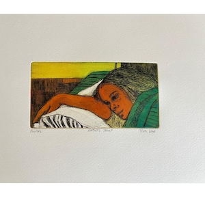 Op de afbeelding: Een kunstafdruk met een vrouw die op een kussen rust. Het kunstwerk heeft een gele en groene achtergrond, met de arm en het gezicht van de vrouw in tinten oranje en bruin. De afdruk is gelabeld met "AWAKE", "ARTIST'S PROOF" en "RUTH LEAF".