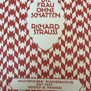 May include: A vintage book cover with a red and white geometric pattern. The title "DIE FRAU OHNE SCHATTEN" and the composer's name, "RICHARD STRAUSS," are displayed in white text. The bottom section reads "VOLLSTANDIGER KLAVIERAUSZUG MIT TEXT BOOSEY & HAWKES."