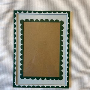 May include: A rectangular picture frame with a scalloped edge design. The frame has a white interior, a light blue border, and a dark green scalloped edge. The frame holds a brown cardboard backing.