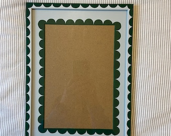 May include: A rectangular picture frame with a scalloped edge design. The frame has a white interior, a light blue border, and a dark green scalloped edge. The frame holds a brown cardboard backing.