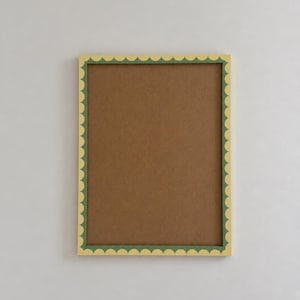 May include: A rectangular picture frame featuring a scalloped edge design. The outer border of the frame is a soft yellow colour, while the inner edge is a dark green. The centre of the frame contains a flat, brown, solid-coloured backing board.