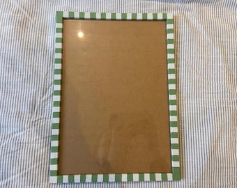 Op de afbeelding: Rechthoekige fotolijst met een groen en wit geblokte rand. De lijst heeft een heldere glazen voorkant en een bruine achterkant. De lijst ligt op een gestreepte stof.