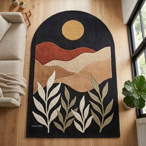 May include: A black area rug with an arched top featuring a landscape design. The rug has a yellow sun, brown and tan mountains, and white and green leaf accents. The rug is on a wooden floor.