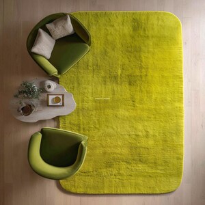 May include: Overhead view of a modern living room setup featuring a large, rectangular, lime green shag rug. Two olive green armchairs and a small, light wood coffee table with decor are arranged on the light wood floor.