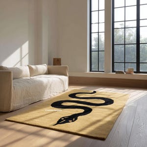 Könnte beinhalten: Rechteckiger Teppich in Senfgelb mit einem schwarzen Schlangenmuster. Der Teppich liegt auf einem Holzboden vor einem cremefarbenen Sofa. Das Design ist ein auffälliges, modernes Element für einen Wohnraum.