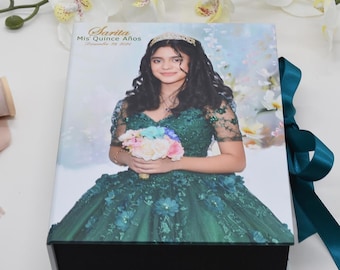 May include: A decorative box featuring a young woman in a green gown, holding a bouquet. The box lid displays the text "Sarita Mis Quince Años" and the date "December 15, 2020". A teal ribbon is tied around the box.