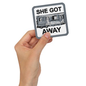 Puede incluir: Una pegatina cuadrada con borde gris y las palabras "SHE GOT AWAY" en negro. La pegatina presenta una ilustración en blanco y negro de un tren subterráneo.