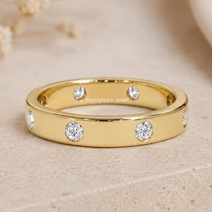 May include: A gold band ring featuring multiple round, clear, bezel-set stones spaced evenly around the circumference. The metal has a polished finish, and the text "royalgleam jewel" is printed in small, dark letters on the inner surface of the band.