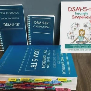 May include: A collection of DSM-5-TR books, including a desk reference, classification guide, and a simplified version. The books are blue and white, with the main text visible on the covers. The books are for the study of mental disorders.