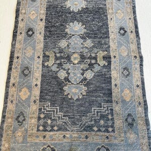 Könnte beinhalten: Ein rechteckiger, dunkelblauer Teppich mit einem Blumenmuster in Hellblau und Beige. Der Teppich hat einen Rand mit geometrischen und floralen Designs. Der Teppich ist wahrscheinlich aus gewebtem Material.