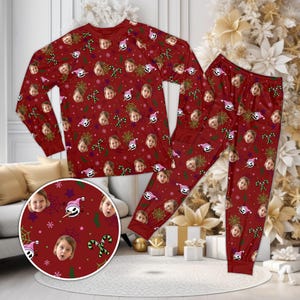 May include: A long-sleeve shirt and pants pajama set in deep red featuring a repeating pattern of a child's face, green spiderwebs, and white and pink character hats. The design includes small green candy canes and white snowflakes throughout.