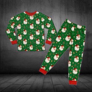 Può includere: Un set di pigiama composto da una maglia a maniche lunghe e pantaloni verdi con una stampa all-over di volti di Babbo Natale, piccoli omini di pan di zenzero e bastoncini di zucchero. Il capo presenta bordi rossi a tinta unita sui polsini.