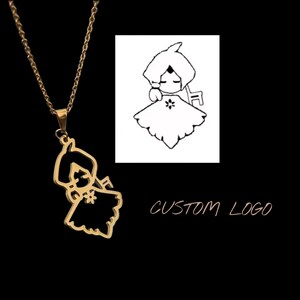 Op de afbeelding: Een goudkleurige metalen ketting met een hanger in de vorm van een gestileerd stripfiguur met een capuchon en een jurk met een klein bloemdetail. De hanger hangt aan een dunne goudkleurige ketting tegen een zwarte achtergrond.