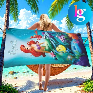 A woman is standing on a beach holding a large towel featuring a mermaid design.
