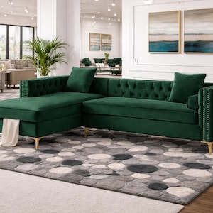 Puede incluir: Un lujoso sofá seccional verde esmeralda con chaise longue, respaldo capitoné y patas doradas. El sofá está adornado con dos cojines a juego y se asienta sobre una alfombra estampada. La habitación es luminosa y espaciosa, con grandes ventanales.