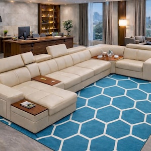 Op de afbeelding: Een grote, beige hoekbank met ingebouwde bijzettafels staat op een blauw tapijt met zeshoekig patroon. De kamer heeft een groot raam, houten meubels en een modern design. De bank heeft verstelbare hoofdsteunen.