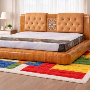 Puede incluir: Una estructura de cama de madera con cabecero acolchado y un colchón. La cama se asienta sobre una plataforma baja. Una alfombra colorida con formas geométricas está frente a la cama. Una lámpara y una planta están en el fondo.