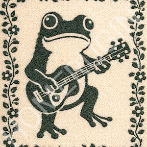 Op de afbeelding: Decoratief tapijt met een grillige kikker die gitaar speelt. De kikker is donkergroen, tegen een crèmekleurige achtergrond en omlijst door een rand van groene bloemenranken en bloemen. Een leuk, muzikaal thema.