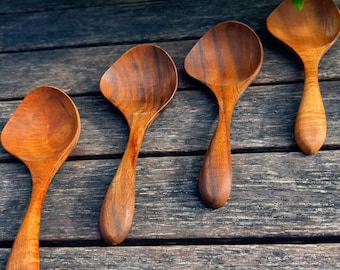 Op de afbeelding: Vier houten lepels met een warme bruine kleur en zichtbare houtnerf liggen op een verweerd houten oppervlak. Elke lepel heeft een unieke, afgeronde kom en een lange, gebogen steel. De lepels variëren enigszins in vorm en grootte.