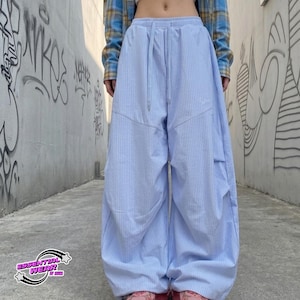 May include: Light blue and white striped pants with a drawstring waist. The pants have a relaxed fit and a unique design. The image also shows a plaid shirt and the text "ESSENTIAL WEAR" in a logo.