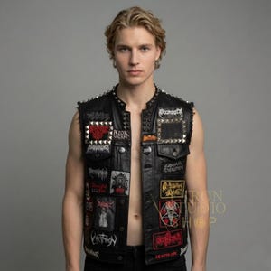 Op de afbeelding: Zwarte leren vest met metalen stud details en patches met bandlogo's en graphics. Het vest heeft een knoopsluiting en een met studs versierde kraag. Patches bevatten rode, witte en zwarte ontwerpen.
