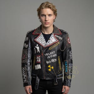 May include: Black leather jacket with silver studs, patches, and text. The jacket features a red collar trim, a chain detail, and multiple patches with text and graphics. The jacket has a belt at the waist.