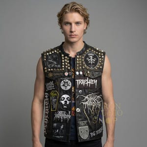 May include: Black leather vest adorned with gold-coloured studs and patches displaying band logos and graphic designs. The vest has a classic biker aesthetic, featuring a sleeveless design and a button-up front. Patches include the text "TRAPHIEM" and "PIG DESTROYER".