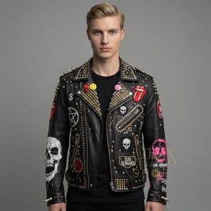 May include: Black leather jacket with gold studs and spikes, featuring patches with skulls, a smiley face, and the Rolling Stones tongue logo. The jacket has a zipper closure and is a bold statement piece.