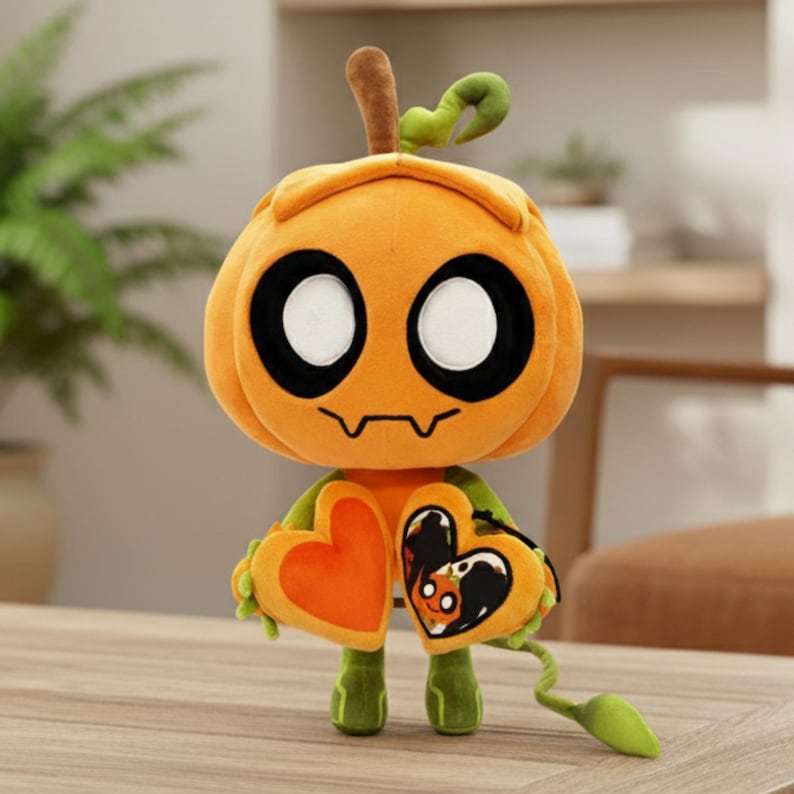 K&ouml;nnte beinhalten: Eine Pl&uuml;schfigur in Form eines K&uuml;rbisses mit einem l&auml;chelnden Gesicht, gro&szlig;en schwarzen Augen und einem Stiel. Sie h&auml;lt zwei herzf&ouml;rmige Objekte, eines orangefarbenes und eines mit einem schwarzen Design. Die Figur hat gr&uuml;ne Beine und einen gr&uuml;nen Schwanz.