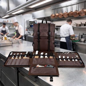Könnte beinhalten: Ein brauner Messer-Rucksack aus Leder mit schwarzen Riemen und Schnallen, der den Schriftzug GRNSH HANDCRAFT trägt. Die Tasche ist geöffnet und zeigt mehrere Innenfächer mit verschiedenen Küchenmessern, Utensilien und einer kleinen Reißverschlusstasche.