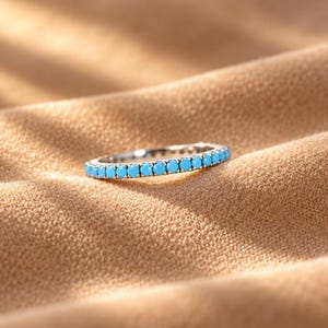 May include: A thin silver-toned band ring featuring a continuous row of small, round, bright turquoise-coloured stones set along the entire outer circumference of the metal band, creating a uniform and symmetrical circular design.