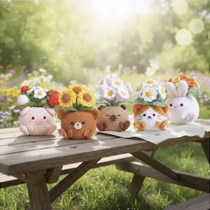 May include: Five crocheted animal planters, each with a different flower arrangement. The planters are shaped like a pig, bear, bear, cat, and bunny. The flowers include daisies, sunflowers, and other colourful blooms. The planters are on a wooden picnic table.