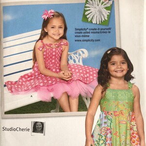 May include: Simplicity sewing pattern number 1821 for girls' dresses. The pattern includes two styles: a pink polka dot dress with a tulle overlay and a green and floral print dress. The pattern is for sizes 3-8.