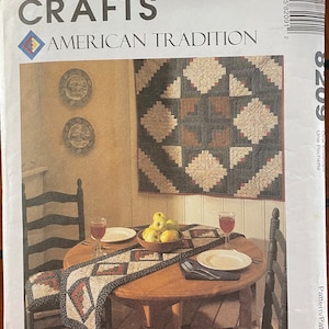 May include: A McCall's Crafts American Tradition quilt pattern for a table runner, pillow, and wall hanging. The pattern features a quilt block design with a mix of brown, beige, and red fabrics.