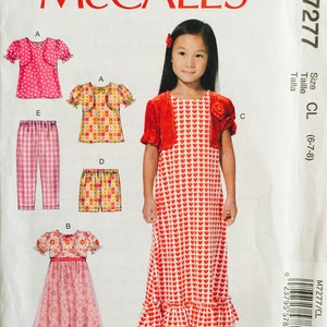 May include: A sewing pattern for a girl's dress, top, and pants. The pattern includes a red and white heart print dress, a red cardigan, a pink and white polka dot top, a plaid pair of pants, and a yellow and white floral print pair of shorts. The pattern is for sizes 6-7-8. The pattern number is M7277.