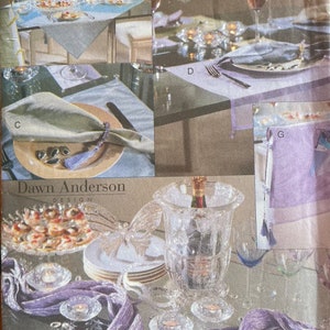 May include: A sewing pattern for a table setting with a purple runner, a green napkin, and a silver napkin ring. The pattern is from Vogue Crafts and is called "Dawn Anderson Design".