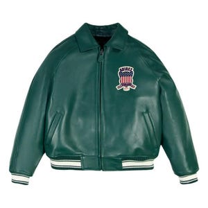 May include: A dark green leather jacket with a collared neckline and a zipper closure. The jacket features a white and black striped trim on the cuffs and hem. An embroidered patch with the word "AVIREX" and a patriotic design is on the chest.