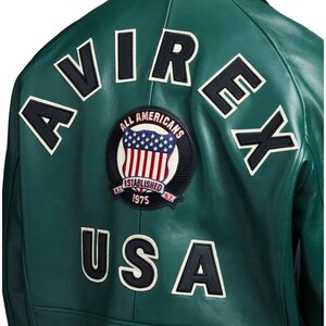 May include: A green leather jacket with white-outlined black lettering spelling "AVIREX" and "USA". A circular patch features the American flag and the words "ALL AMERICANS ESTABLISHED 1975 N.Y."