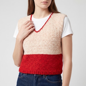 May include: A knitted vest with a V-neck design. The vest features a color block design with a red bottom, a light pink middle section, and a textured cream-colored top. The neckline is trimmed with red stitching.