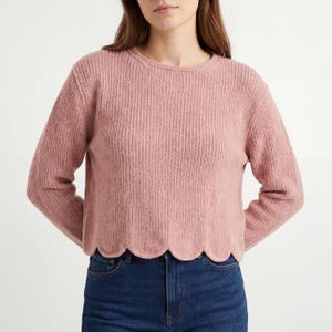 Può includere: Un maglione color rosa antico con una trama a coste e scollo tondo. Il top a maniche lunghe ha un orlo smerlato. La modella indossa jeans blu scuro.