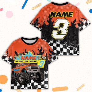 May include: Orange and black graphic t-shirt featuring a monster truck design with the text "READY TO CRUSH" and the number 3. The shirt has a checkered flag pattern and the word "NAME" on the back.