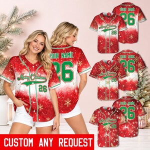 Può includere: Una maglia da baseball rossa e bianca con un motivo a fiocchi di neve sfumato, finiture verdi, il testo Merry Christmas e il numero 26. Il retro mostra il testo YOUR NAME sopra il numero 26 in verde con un contorno bianco.