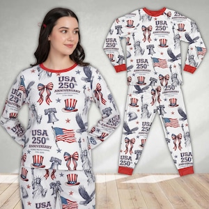 Könnte beinhalten: Weißes Pyjama-Set mit rotem Besatz, das den 250. Jahrestag der USA feiert. Das Muster umfasst Flaggen, Schleifen, Freiheitsglocken und die Freiheitsstatue. Langärmliges Oberteil und Hose sind sichtbar.