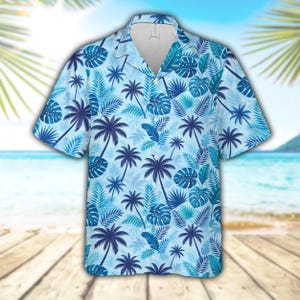 May include: A short-sleeve button-down shirt featuring a light blue background with a repeating pattern of dark blue palm trees and various tropical leaves. The garment has a classic collar, a front button placket, and a straight hemline.
