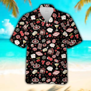 May include: A black short-sleeve button-down shirt featuring an all-over print of casino-themed icons including slot machines, roulette wheels, playing cards, dice, cherries, martini glasses, and red number seven symbols with the word Casino.