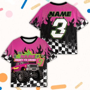 May include: Pink and black short-sleeved t-shirt with a monster truck graphic. The shirt features the text "NAME" and the number "3" in green and white. Flames and a checkered flag design are also present.