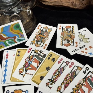 Puede incluir: Un juego de cartas con ilustraciones pixeladas. Las cartas presentan diferentes palos y figuras, incluyendo reyes, jotas y comodines. La paleta de colores incluye tonos de rojo, dorado y azul.