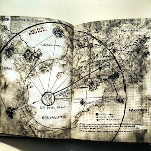 May include: Open book with a detailed map illustration. The map features circular patterns, lines, and text including "HSB - HELICOPTER FUEL RANGE", "AUX FUEL RANGE 500 KM", and country names like Iran, Afghanistan, and Pakistan. The style is a mix of hand-drawn and technical.